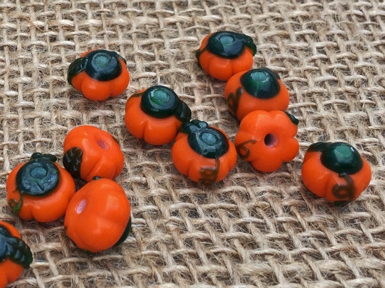 May include: A collection of orange and green glass pumpkin beads. The beads are about 1 inch in diameter and have a glossy finish.