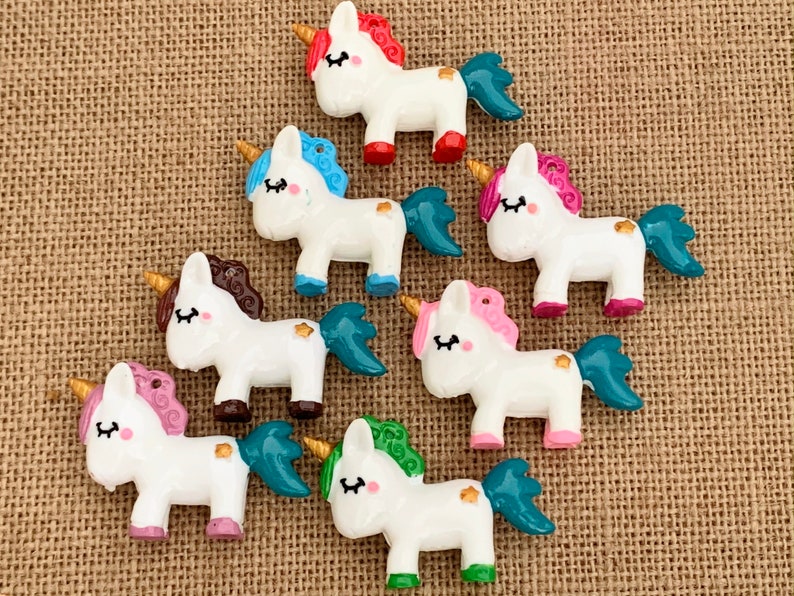 May include: Seven colourful unicorn charms with white bodies, gold horns, and different coloured manes and tails. The charms are made of resin and have a glossy finish.