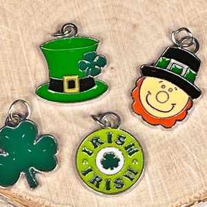 Peut inclure: Quatre breloques en métal sur le thème irlandais. Les breloques sont vertes, noires, orange et blanches. Une breloque est un chapeau de lutin vert, une autre est un trèfle vert, une autre est un cercle vert avec le mot "Irish" écrit autour, et la dernière est un lutin de dessin animé avec un chapeau noir et des cheveux orange.