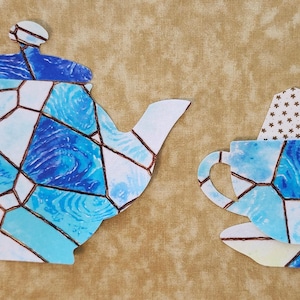 May include: A blue and white teapot and teacup with a stained glass design. The teacup has a tea bag hanging from it.