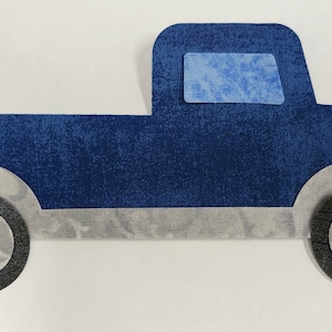 May include: A blue felt toy truck with gray wheels and a blue window. The truck is a simple design with no details.