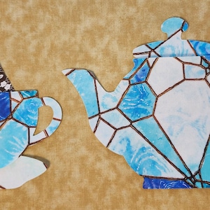 May include: A blue and white teacup and teapot with a stained glass design. The teacup has a brown tea bag inside.