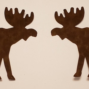May include: Two brown moose silhouettes facing each other. The moose have large antlers and are cut from a flat material. The background is a plain, off-white color. The moose are likely decorative items.