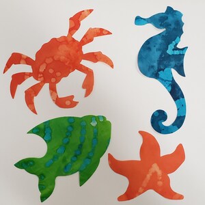 May include: Four colorful felt cutouts of sea creatures: a red crab, a blue seahorse, a green fish, and an orange starfish.
