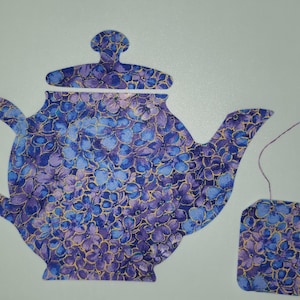 May include: A blue and purple floral patterned teapot with a matching tea bag hanging from the spout.