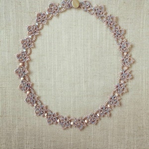 May include: A delicate necklace made of intricate lacework in shades of pink and gray. The necklace features small, round beads and a clasp closure.