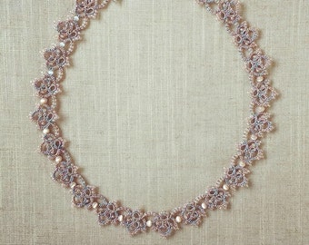 May include: A delicate necklace made of intricate lacework in shades of pink and grey. The necklace features small, round beads and a clasp closure.