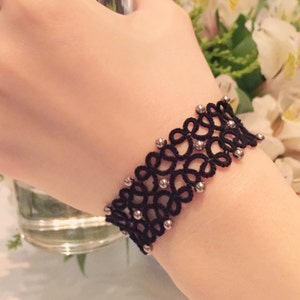 May include: A black lace bracelet with silver beads. The bracelet is delicate and intricate, with a floral design.