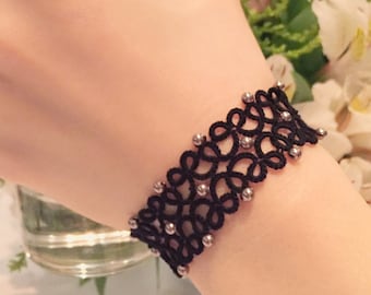 May include: A black lace bracelet with silver beads. The bracelet is delicate and intricate, with a floral design.
