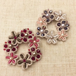 May include: Two crocheted flower wreaths with beaded accents. One wreath features red and pink beads, while the other has purple and pink beads.