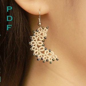 May include: A cream-coloured, crescent-shaped earring with a delicate, lace-like design. The earring is adorned with small, dark beads along the curve. The text "PDF PATTERN" is visible in teal on the left side. The earring hangs from a silver hook.