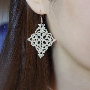 May include: White lace earrings with a diamond shape and silver hooks. The earrings are delicate and intricate.