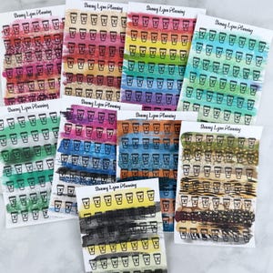 May include: Nine sheets of planner stickers featuring rows of black coffee cup icons with heart details. Each sheet displays horizontal brushstroke backgrounds in various colors, including pink, yellow, green, blue, and brown. Text reads Sammy Lynn Planning.