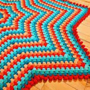 以下が含まれることがあります： オレンジ、赤、ターコイズ、ブルーの繰り返しパターンを持つ、マルチカラーの星形クロシェラグ。ラグは白い縁取りがあります。