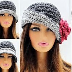 Pode incluir: Chapéu cloche de crochê em tons de cinza e preto, com um detalhe floral rosa. O chapéu é no estilo flapper dos anos 20. O texto na imagem diz "Roaring 20's Flapper Hat."