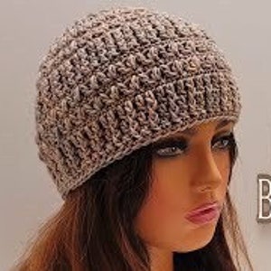 May include: A crocheted beanie and scarf set in a light brown color. The beanie is on a mannequin's head and the scarf is not visible in the image.