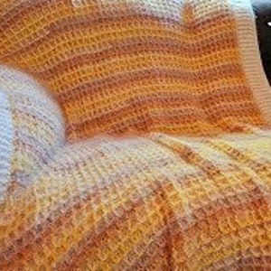 May include: A crocheted throw blanket with a waffle stitch pattern in shades of white, yellow, and orange. The blanket is draped over a brown leather chair. The text "L'Eggo My Eggo Throw" is visible in the upper right corner of the image.