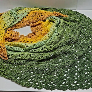 May include: A handmade crochet shawl in shades of green, yellow, and brown. The shawl features a spiral design with openwork detailing. The text "Whispers In My Head" is visible in the upper right corner. This item is perfect for adding a touch of handmade charm to any outfit.