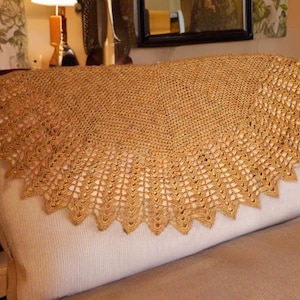 May include: A gold crocheted shawl with a scalloped edge, draped over a white couch.