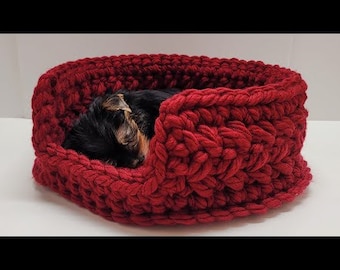 May include: A red crocheted dog bed with a small black and brown dog sleeping inside.