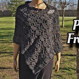 Puede incluir: Un poncho de crochet negro con un patrón de encaje. El poncho lo lleva una persona de pie en un campo de hierba.
