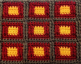 Puede incluir: Primer plano de un textil tejido a ganchillo con un patrón repetitivo de cuadrados. Cada cuadrado presenta un centro amarillo, enmarcado por un borde rojo y delineado con hilo marrón oscuro. La textura general es densa y visualmente atractiva.