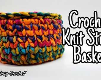 May include: A colorful crocheted basket made with a knit stitch. The basket is made with a variety of colors, including orange, red, blue, green, and yellow. The basket is sitting on a white surface. "Bag-O-Day Crochet" is written in the bottom left corner of the image. The text "Crochet Knit Stitch Basket" is written in large, white letters in the upper right corner of the image.