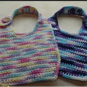 May include: Two handmade crochet bibs. One bib features a pastel color scheme of pink, yellow, and blue. The other bib has a blue, purple, and white color scheme. Each bib has a strap with a wooden button closure.