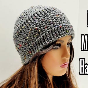 May include: A gray crocheted beanie with colorful flecks. The beanie is worn by a person with long brown hair.
