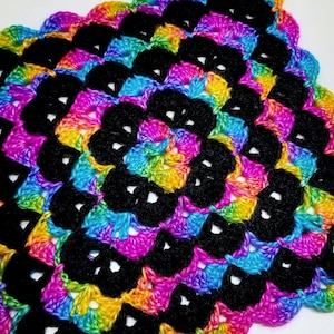 May include: A colorful crochet square with a black center. The square is made with a rainbow yarn and has a scalloped edge.