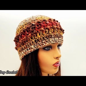 May include: A crocheted beanie hat in shades of brown, orange, and yellow. The hat has a textured stitch pattern and a slouchy fit.