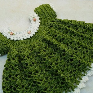 May include: A green crocheted baby dress with a white crocheted collar and pink flower embellishments.
