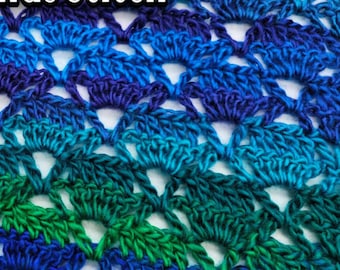 May include: Close-up of a crocheted fabric with a gradient of blue, teal and green colours. The fabric is made with a repeating pattern of small, rounded shapes.