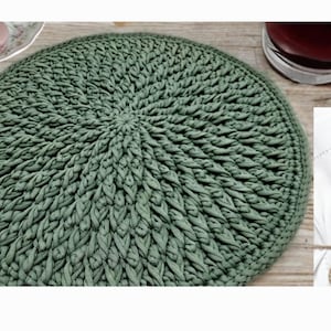 May include: A green crocheted round placemat with a circular pattern. The placemat is made of thick yarn and has a textured surface.