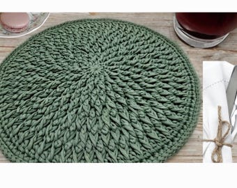 May include: A green crocheted round placemat with a circular pattern. The placemat is made of thick yarn and has a textured surface.