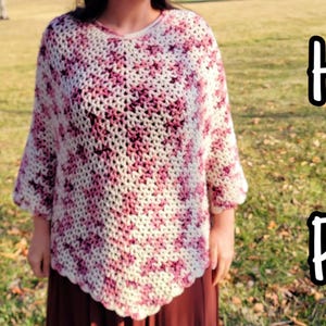May include: A crocheted poncho with a pink and white color pattern. The poncho has a scalloped hem and is worn by a person standing in a grassy field.