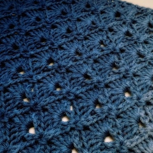 May include: A close-up of a blue crocheted blanket with a gradient pattern. The blanket is made with a stitch that creates a textured, openwork design.