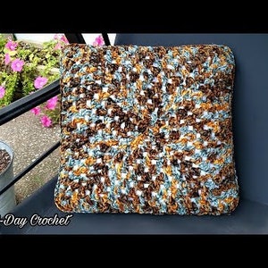 May include: A crocheted pillow with a brown, blue, and white geometric pattern. The pillow is sitting on a black metal chair.