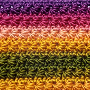 May include: Multicolored crocheted fabric with a repeating flower pattern. The fabric is made with a gradient of purple, pink, orange, green, and yellow yarn.