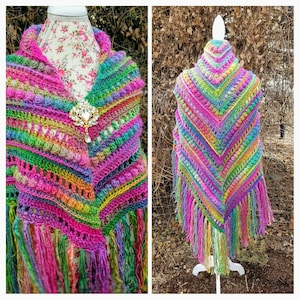 May include: A colorful crochet shawl with a fringe border. The shawl is made with a variety of colors, including pink, green, purple, and yellow. It is displayed on a white mannequin.
