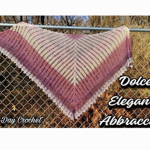 May include: A crocheted shawl in shades of pink and white with a delicate lace border. The shawl is draped over a chain link fence and the text "Dolce Eleganza Abbracciata" and "Bag-O-Day Crochet" is visible.