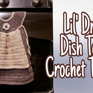 May include: A crocheted dish towel shaped like a dress with a brown and beige color scheme. The towel has a flower embellishment and is hanging on an oven door. Lil' Dress Dish Towel Crochet Tutorial.