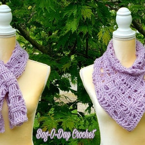 May include: Two crocheted scarves in a light purple color. One scarf is tied around a mannequin's neck, while the other is draped over the mannequin's shoulders. The scarf draped over the shoulders has a decorative button.