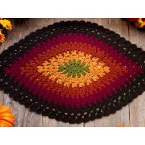 May include: A crocheted oval rug with a black border and a multi-colored center. The center is a gradient of red, orange, yellow, and green.