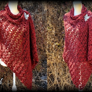 May include: A maroon crocheted shawl with a lacy pattern, draped over a mannequin. The shawl has a cowl neck and is displayed against a backdrop of brown branches.