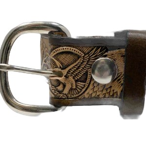 Peut inclure: Une ceinture en cuir marron avec une boucle argent&eacute;e et un motif d'aigle. La boucle est de forme ovale simple avec une finition lisse. Le motif de l'aigle est gaufr&eacute; dans le cuir et pr&eacute;sente des d&eacute;tails complexes.