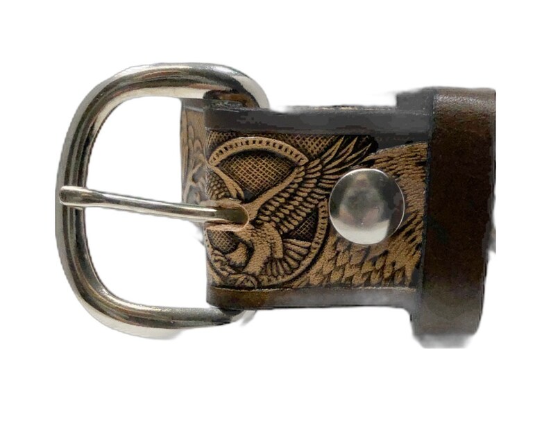 Peut inclure: Une ceinture en cuir marron avec une boucle argent&eacute;e et un motif d'aigle. La boucle est de forme ovale simple avec une finition lisse. Le motif de l'aigle est gaufr&eacute; dans le cuir et pr&eacute;sente des d&eacute;tails complexes.