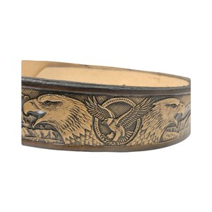 Peut inclure: Une ceinture en cuir marron avec un motif en relief de deux aigles aux ailes d&eacute;ploy&eacute;es. Les aigles sont dans un cercle avec un plus petit aigle au centre.