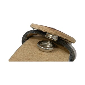 Peut inclure: Gros plan sur une ceinture en cuir marron avec une fermeture &agrave; pression m&eacute;tallique. Le fermoir est ouvert, r&eacute;v&eacute;lant l'anneau m&eacute;tallique &agrave; l'int&eacute;rieur.