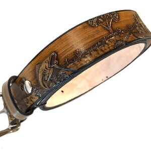 May include: A brown leather belt with a tooled design of a fish jumping out of the water. The belt has a silver buckle.